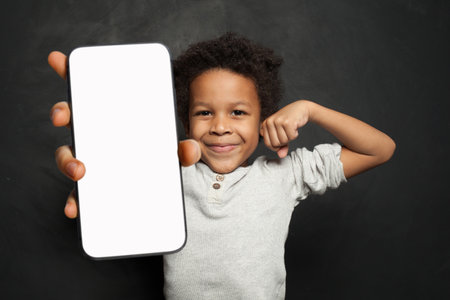 Little happy fun boy 6-7 years old holding showing mobile cell phone with blank screen workspace area on black backgroundの写真素材