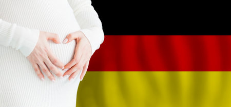 Demographics, pregnancy and love baby in Germany concept. Pregnant woman making heart against her stomach on German flag background.の写真素材