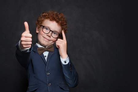 Clever school kid young boy in glasses showing thumb up on black background with copy spaceの写真素材