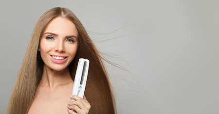Happy woman with hair straightener iron in studio isolated on white background. Haircare, wellness and young female model with flat iron for salon treatment hairstyle, styling and hair careの写真素材
