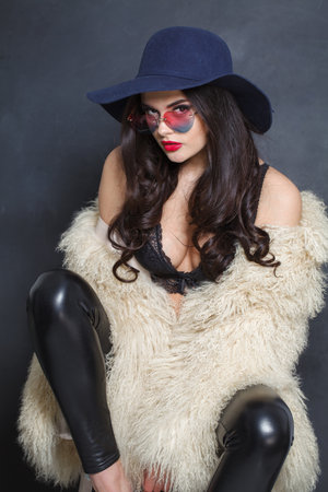 Charming woman with red lips make-up and long wavy hair wearing blue hat against dark studio wall backgroundの写真素材