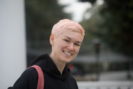 Laughing woman with short hair smiling, standing and looking at camera, outdoors portrait