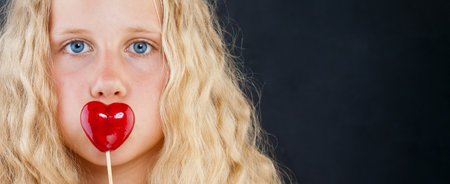 Close-up studio portrait of young child girl holding red heart on black backgroundの写真素材
