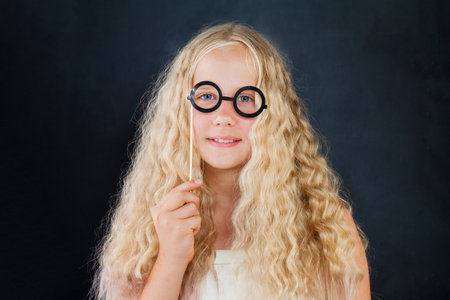 Attractive young girl posing with photo booth props glasses on black backgroundの写真素材