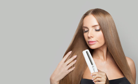 Perfect woman with long hair using a straight hair iron and doing a hairstyle, beauty, care and fashion conceptの写真素材