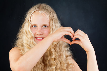 Pretty young girl making heart on black background portraitの写真素材