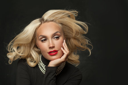 Stylish blond woman with makeup and perfect wavy hair posing on black studio wall background, portraitの写真素材