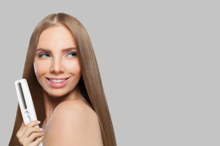 Cheerful woman with long hair using a straight hair iron and doing a hairstyle, beauty, care and fashion conceptの写真素材