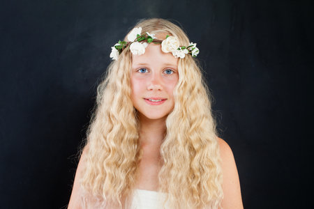 Beautiful blond child girl with fashion flower decor on black background portraitの写真素材
