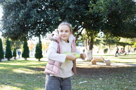 Smiling happy girl child playing frisbee in a sunny, green outdoor setting, exemplifying carefree and playful moments in a kid's life.の写真素材
