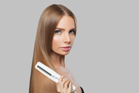 Young fashion model woman using hair straighteners iron on white background. Harstyle, hair care, beauty salon and treatment conceptの写真素材