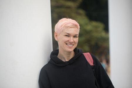 Joyful mid adult woman in city park. Mature traveler with elegant short haircut wearing black hoodie and jacket outdoorsの写真素材