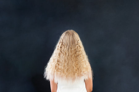 Blond hair girl. Back of young female model with long wavy healthy hair on black backgroundの写真素材