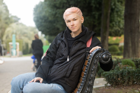 Resting mid adult woman in city park. Mature traveler with elegant short haircut wearing black hoodie and jacket outdoorsの写真素材