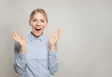 Surprised blond woman wearing shirt standing with hands up and looking at camera, portraitの写真素材