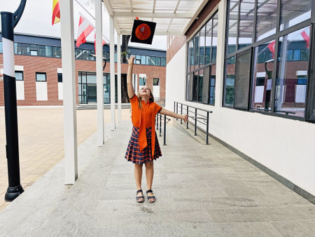Happy elementary student schoolgirl celebrating her graduation day while throwing her cap up in the airの写真素材