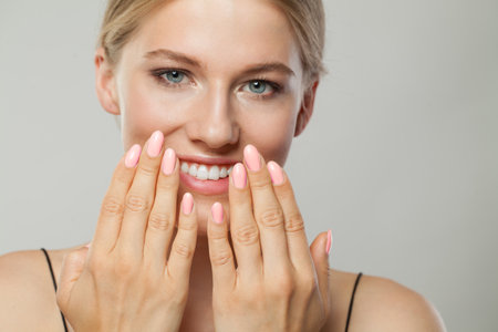 Close-up studio portrait of beautiful woman with pink nail polish on her handの写真素材