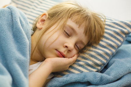 Sleeping child in bed on a pillow. Adorable little girl indoor portraitの写真素材
