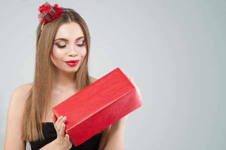 Cheerful young happy woman holding gift present box on gray studio wall background, fashion beauty portraitの写真素材