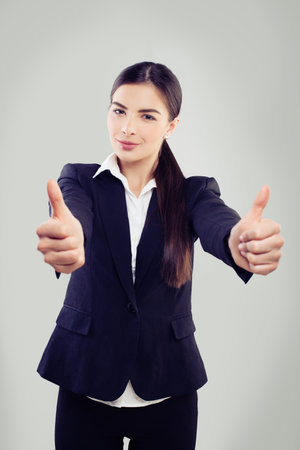 Successful business woman looking at camera, smiling and holding thumb up on white backgroundの写真素材
