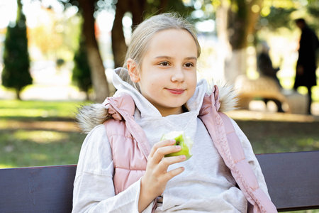 Resting young girl eating green apple outdoors, portrait. Child 11 years oldの写真素材