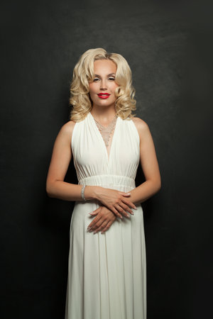 Nice blond woman with makeup and perfect wavy hair posing on black studio wall background, portraitの写真素材
