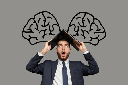 Emotional shocked businessman in suit with laptop on his head on gray background and with drawing of brains above his head. Concept of thinking, idea, troubleshootingの写真素材