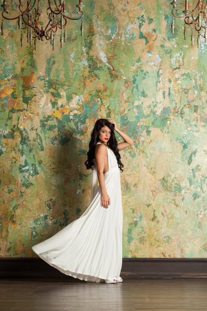 Beautiful fashion woman in white silk dress posing in perfect interiorの写真素材