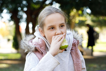 Beautiful child eating apple fruit outdoors. Young girl 10 years oldの写真素材