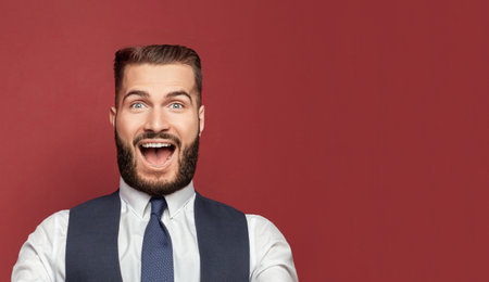 Young man with a surprised happy expression won on red studio background. Human facial emotions and expression conceptの写真素材