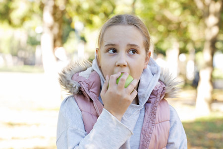 Child girl biting green apple outdoors. Healthy playful kid portraitの写真素材