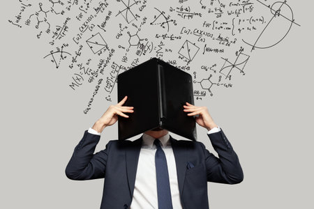 Frustrated stressed businessman hiding his head under laptop in office with mathematical formulas on the background. Concept of money, education and enterpreneurshipの写真素材