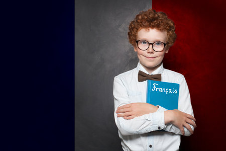Young school boy holding book with the inscription Francais in France standing against French flag background. Education and study language in France conceptの写真素材