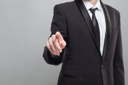 Businessman in black suit poingting on camera on the gray plain backgroundの写真素材
