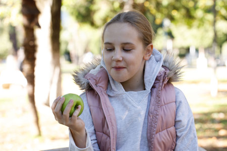 Happy young girl with apple fruit in park. Child 10 years oldの写真素材
