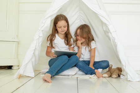 Adorable child sisters using tablet computer sitting on floor at homeの写真素材