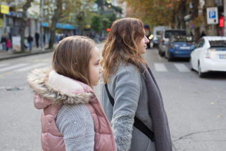 Outdoors portrait of mother and daughter hold each other's hand and cross the road at a crosswalkの写真素材