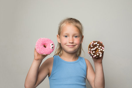 Pretty child girl holding testy donut. Cute little girl with sweet food indoorの写真素材