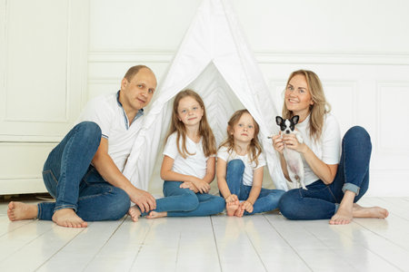 Indoor portrait of happy family having fun with puppy dog pet at home. Father, mother and two daughtersの写真素材