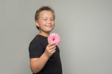 Smiling child boy holding testy donut. Kid in black t-shirt with sweet food indoorの写真素材