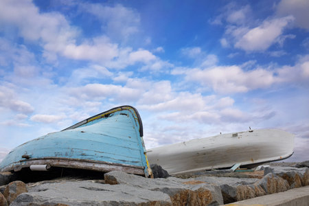 Old Fishing Boats on Rocky Shore Under Cloudy Skyの写真素材