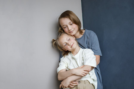 Smiling sibling children having fun at home while standing against blue and white wall background. Little girl 6 years old and boy 11 years oldの写真素材
