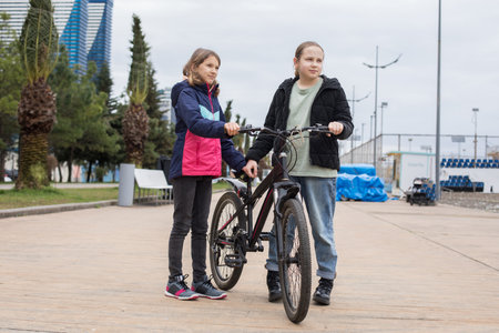 Cheerful young girls talking and walking together. Children with bikes outdoors