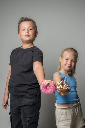Joyful children holding chocolate glazed donut indoor. Happy kids with sweet food portraitの写真素材
