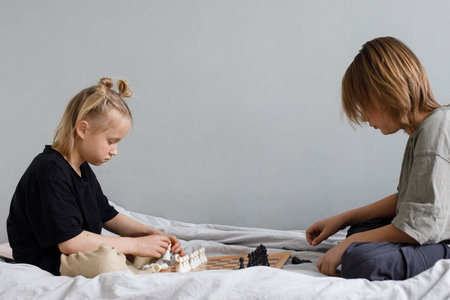 Cheerful little girl and young boy have a nice game. Sibling playing chess on the bed at home togetherの写真素材
