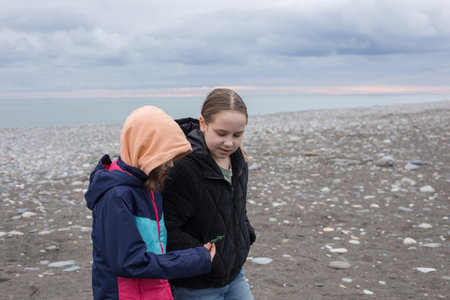 Two young girls children in season jacket walking on sea beach