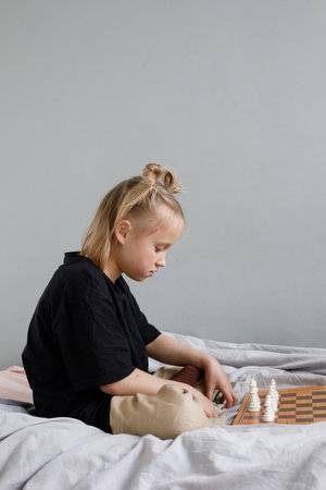 Pensive little child girl playing chess while spending leisure time at homeの写真素材