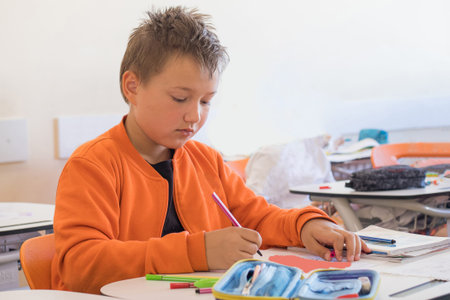 Young boy student sitting at desk writing in notebook in school classroom. School child learning