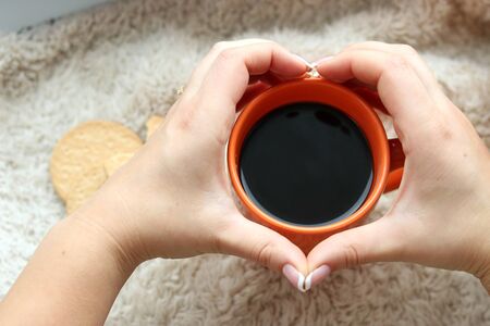 Girl's hands hold a cup of orange with coffeeの写真素材