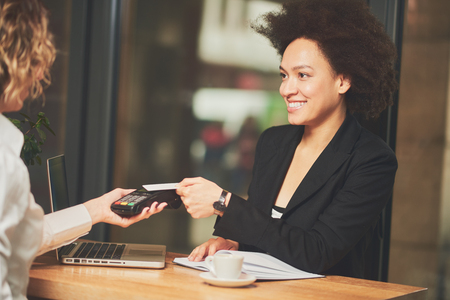 Mixed race woman in coffee shop having coffee and using credit card for paying onlineの写真素材